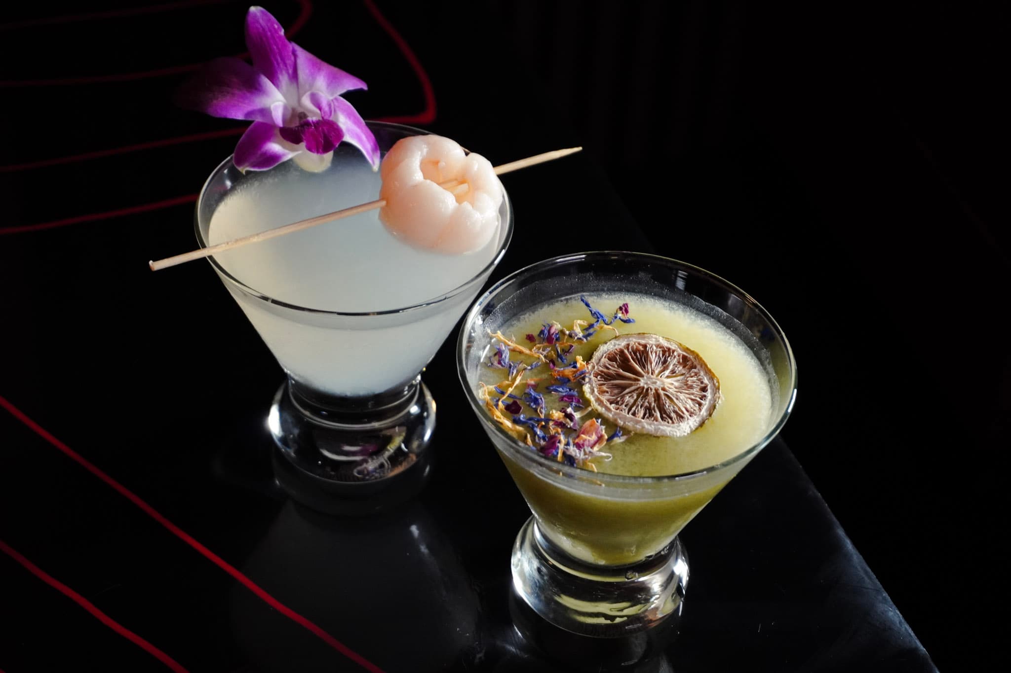 Signature cocktails with floral garnishes against a dark speakeasy backdrop.