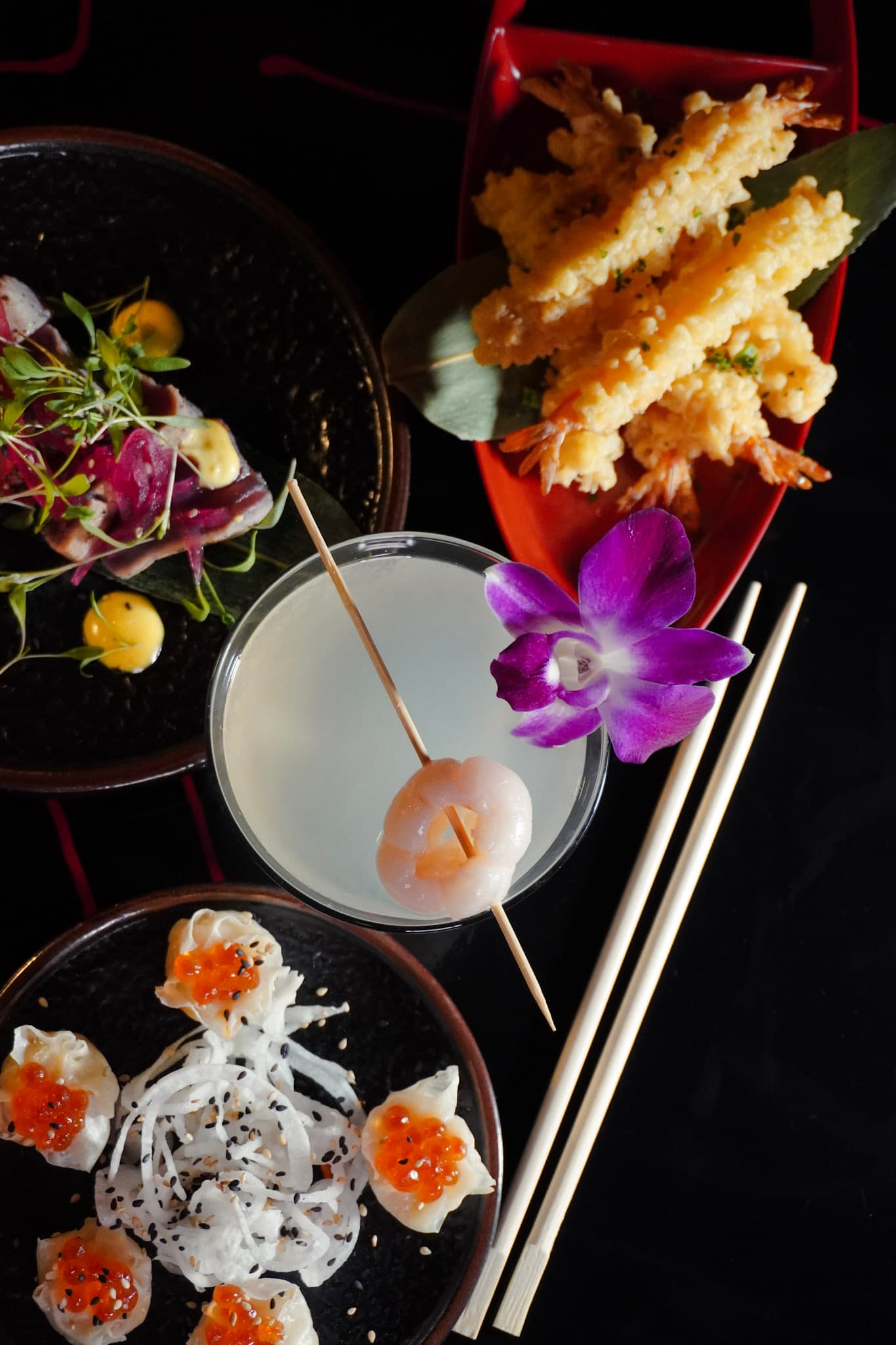 A vertical spread of tempura, sashimi, and cocktail service with dramatic lighting.