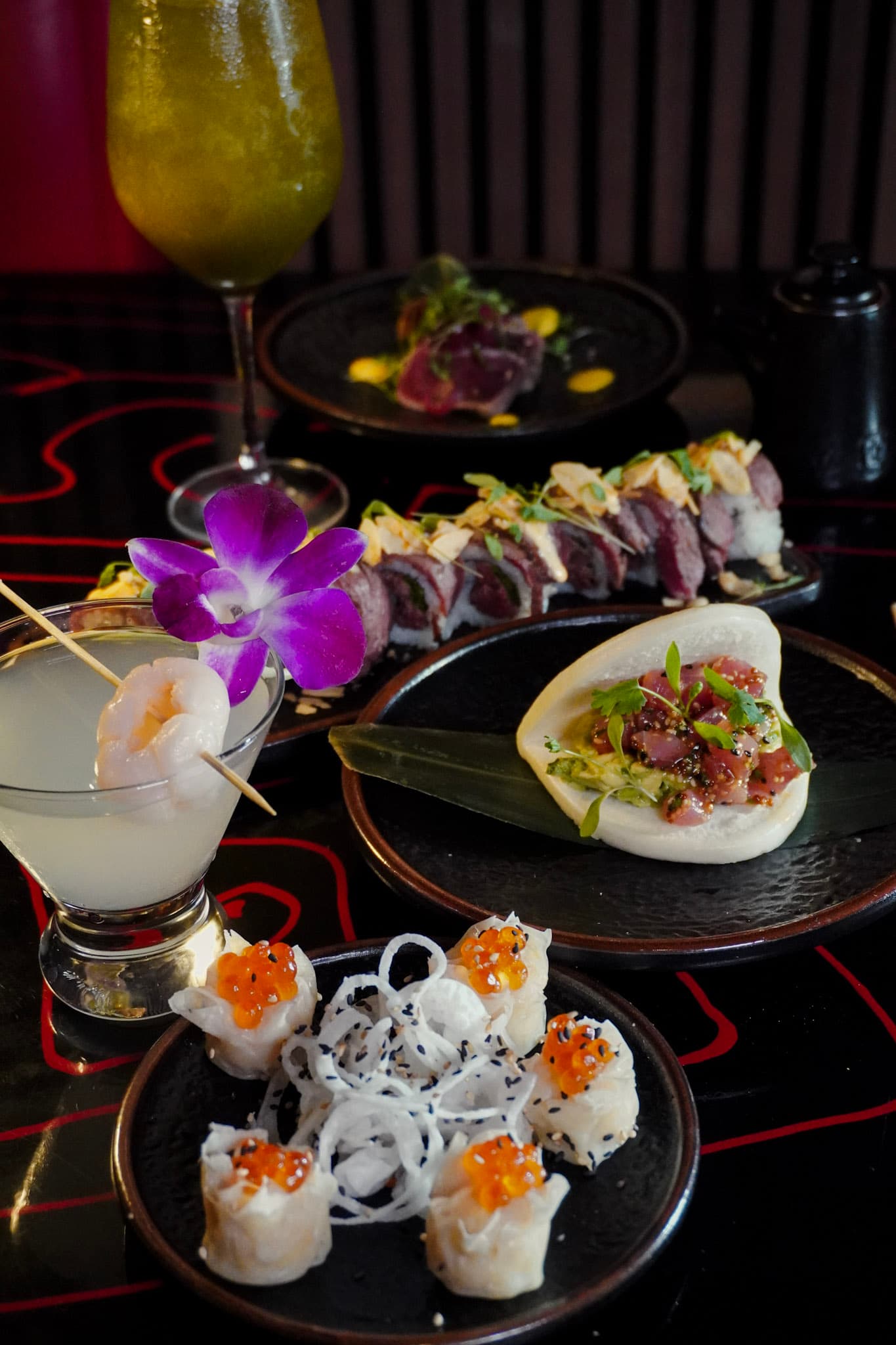 A cocktail and premium sushi dishes staged on a dramatic black table.