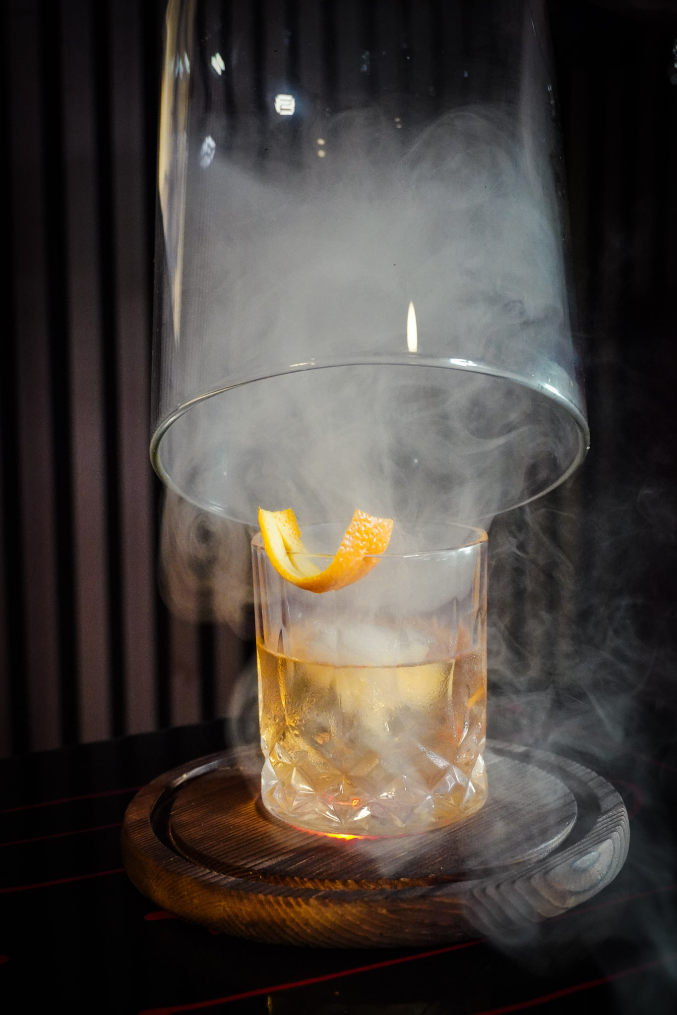 A smoky cocktail under a glass cloche on a wooden board.
