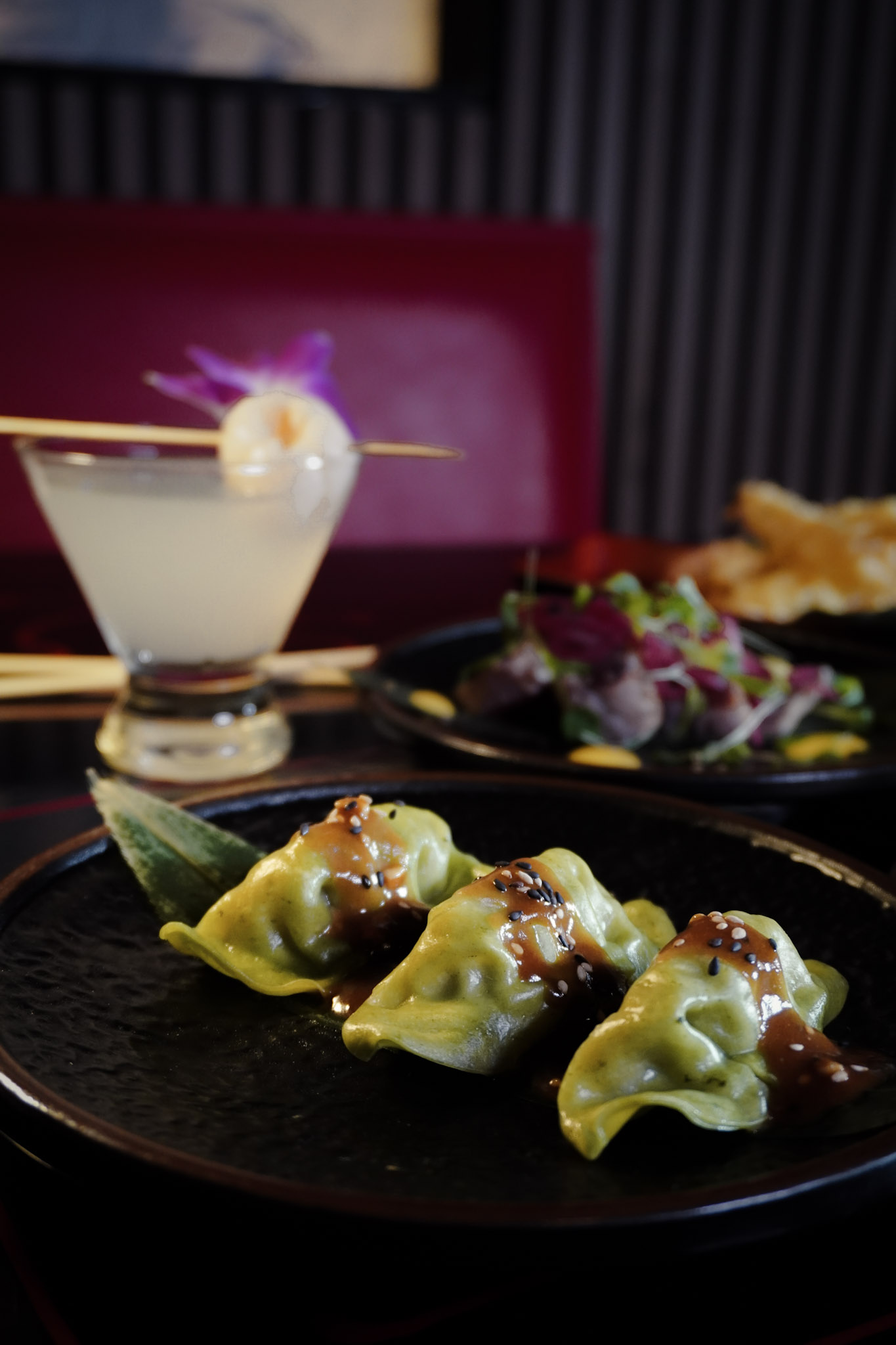A moody table scene with gyoza, cocktails, and layered plating.